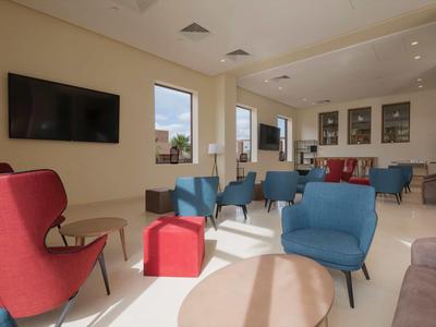 Světlý salonek s barevnými křesly, pohovkou a televizí na stěně.