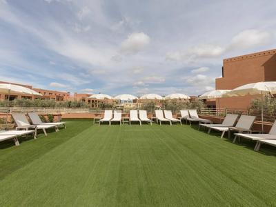 Sluneční terasa s lehátky a slunečníky na zelené umělé trávě pod zataženou oblohou.