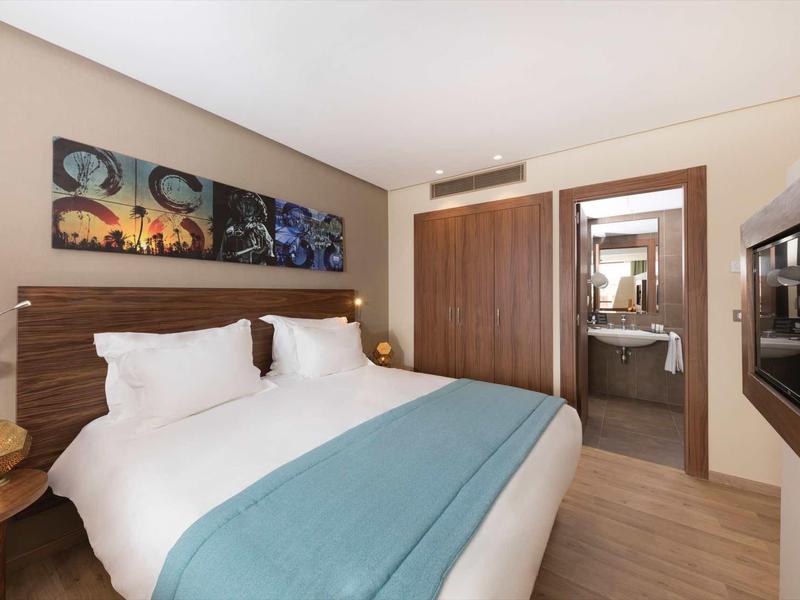 Chambre d'hôtel moderne avec lit double, jeté bleu et vue sur la salle de bain.