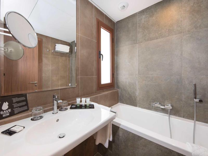 Salle de bain moderne avec baignoire, grand miroir et fenêtre laissant passer la lumière naturelle.