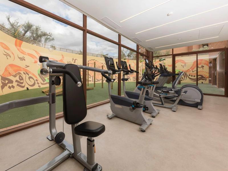 Salle de fitness bien équipée avec vue sur un mur de verre peint à l'hôtel.