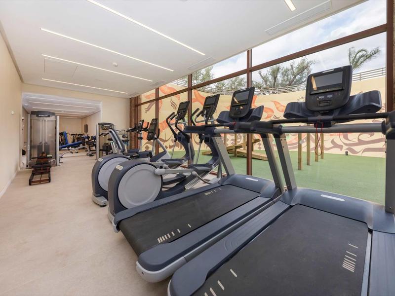 Salle de sport moderne avec tapis de course et autres équipements devant de grandes fenêtres donnant sur la verdure.
