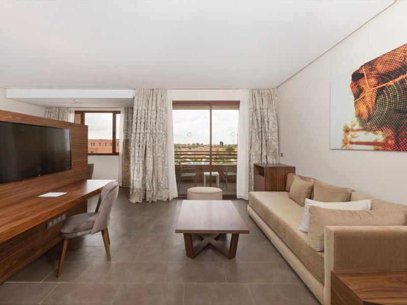 Chambre d'hôtel moderne avec canapé, TV, bureau et balcon avec vue.