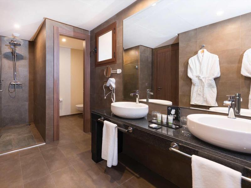 Salle de bains moderne avec douche à l'italienne, doubles lavabos et peignoirs blancs.