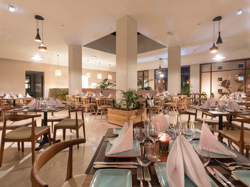 Restaurant d'hôtel élégant avec tables en bois, nappes roses et chaises modernes sous lumière chaude.