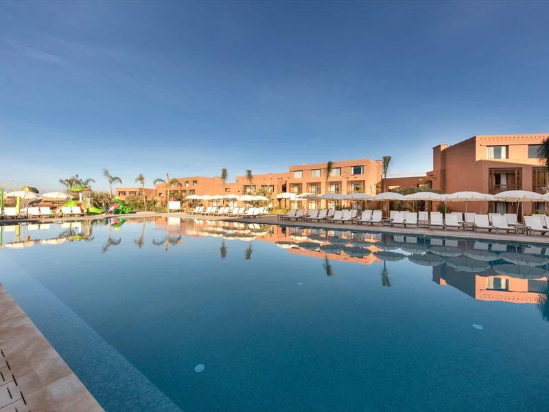 Grand piscine extérieure devant un bâtiment hôtelier à plusieurs étages sous un ciel clair.