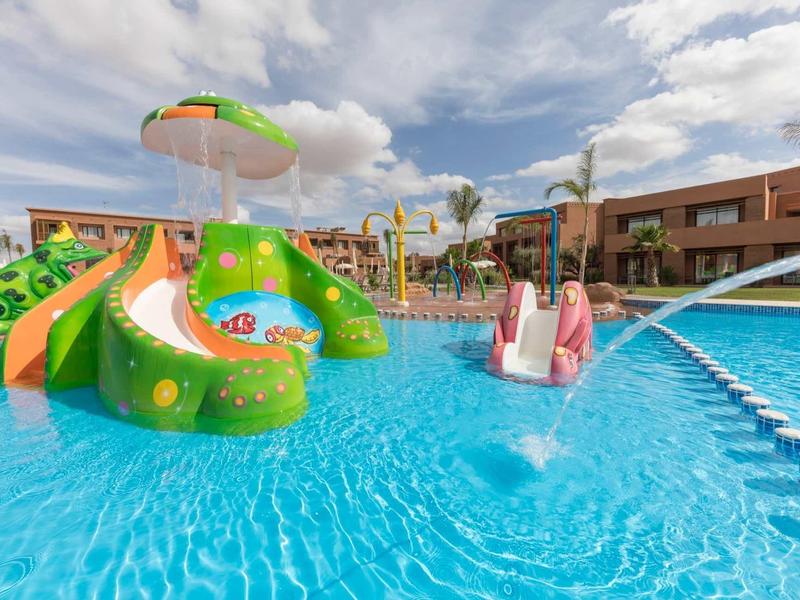 Aire de jeux aquatique colorée avec toboggans et fontaines dans une piscine d'hôtel par temps ensoleillé.