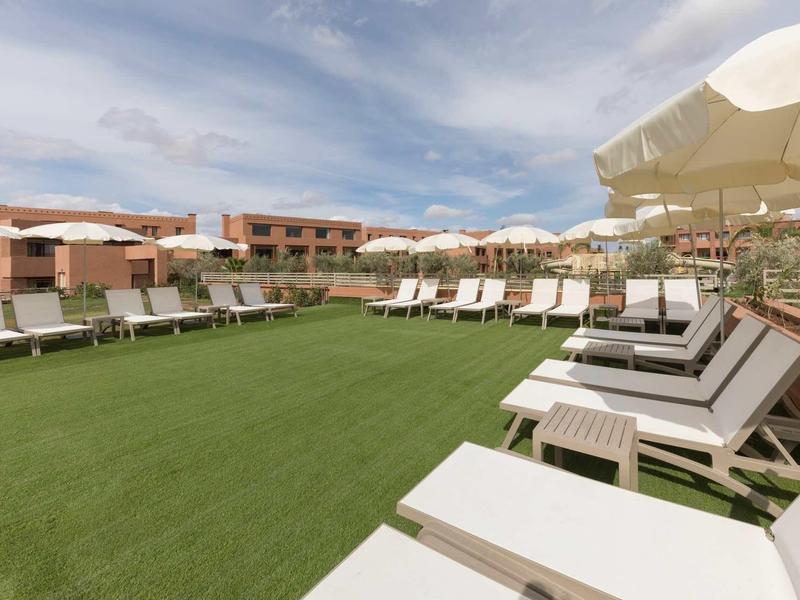 Grande piscine avec chaises longues et parasols sur herbe verte sous un ciel bleu.