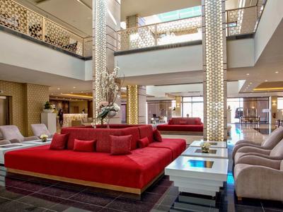 Bright modern hotel lobby with red and beige seating and large windows.