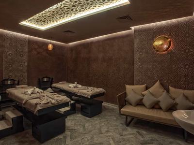 Przyciemnione pomieszczenie spa z dwoma stołami do masażu i wygodną sofą.