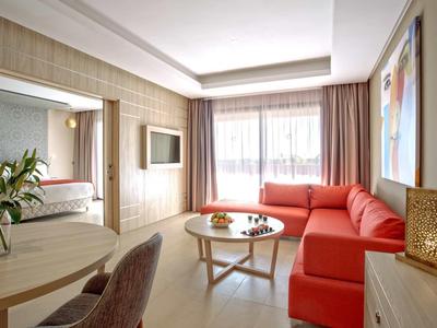 Jasny salon z czerwonymi kanapami, okrągłym stołem i dużym oknem z zasłonami.