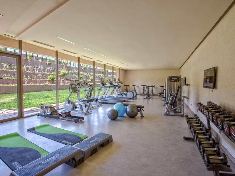 Jasna siłownia z bieżniami, hantlami i sprzętem fitness obok dużych okien.