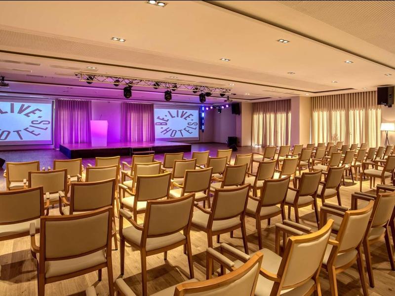 Duża nowoczesna sala konferencyjna z rzędami krzeseł i dwoma ekranami projekcyjnymi.