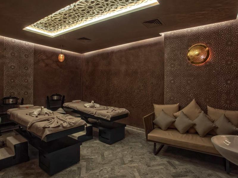 Przyciemnione pomieszczenie spa z dwoma stołami do masażu i wygodną sofą.