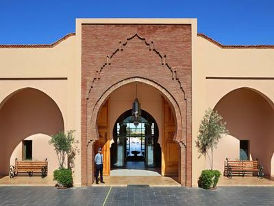 Vstup do hotelu s arabským obloukem, lucernami a lavičkami pod jasnou oblohou.