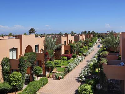 Řada rodinných domů podél cesty lemované palmami za jasné oblohy.