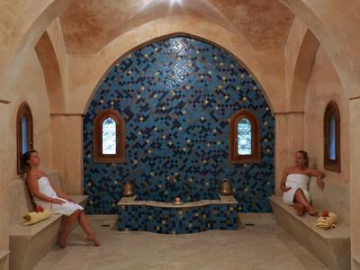Relaxační místnost se dvěma osobami, obloukovými okny a modrou mozaikovou stěnou.