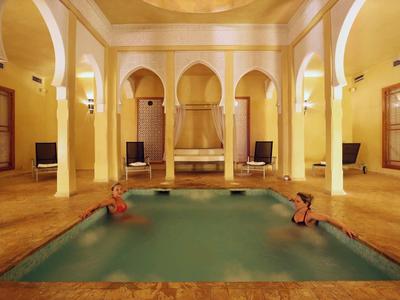 Vnitřní bazén v elegantní místnosti se sloupy a teplými žlutými tóny, dvě osoby relaxují ve vodě.