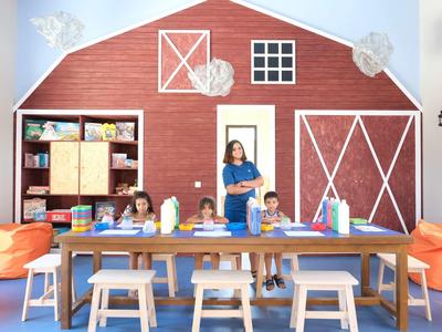 Děti sedí u stolu v místnosti s velkou červenou dekorací na stěně ve tvaru stodoly.