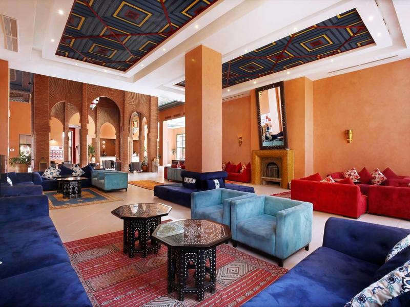 Elegantní hotelová lobby s barevnými pohovkami, koberci a dekorativními vzory na stropě.