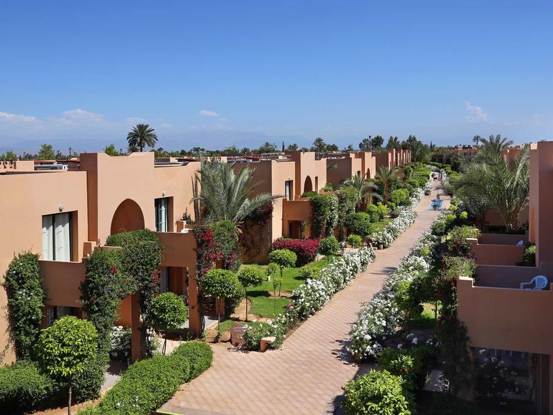 Řada rodinných domů podél cesty lemované palmami za jasné oblohy.