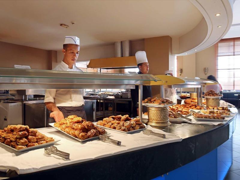 Bufet s různými pečivy a dvěma kuchaři v hotelové kuchyni.