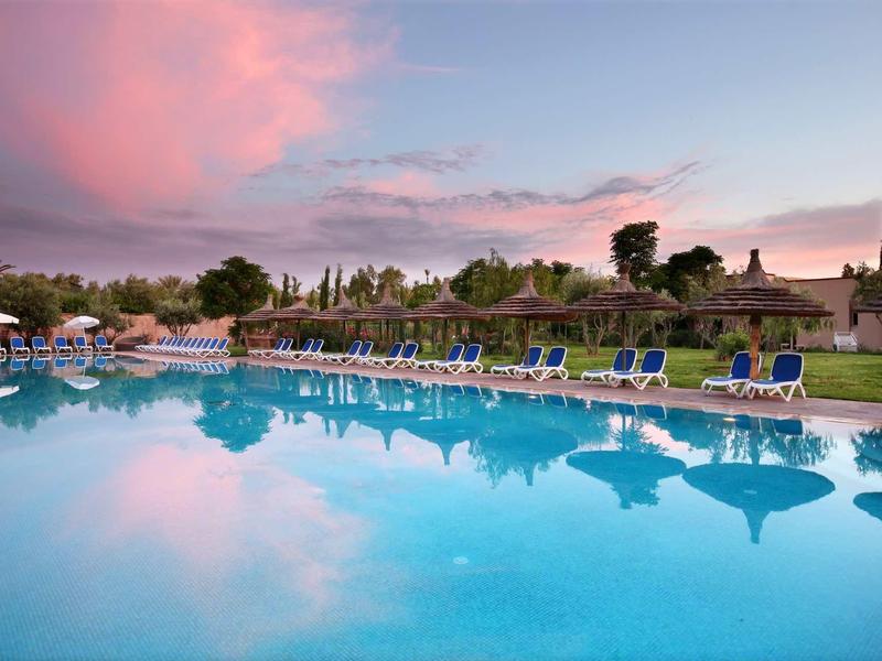 Velký hotelový bazén s lehátky a slunečníky při západu slunce.