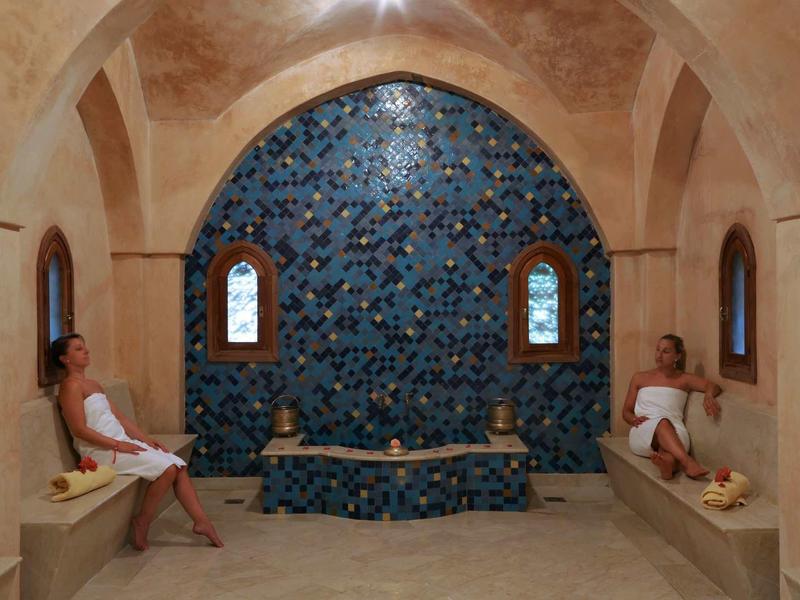 Relaxační místnost se dvěma osobami, obloukovými okny a modrou mozaikovou stěnou.