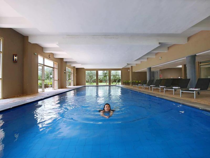 Vnitřní bazén s plavcem a lehátky po straně.