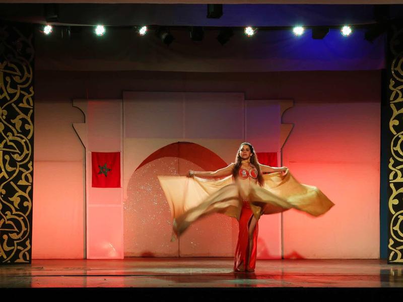 Břišní tanečnice tančí na pódiu s orientálním pozadím za teplého osvětlení.
