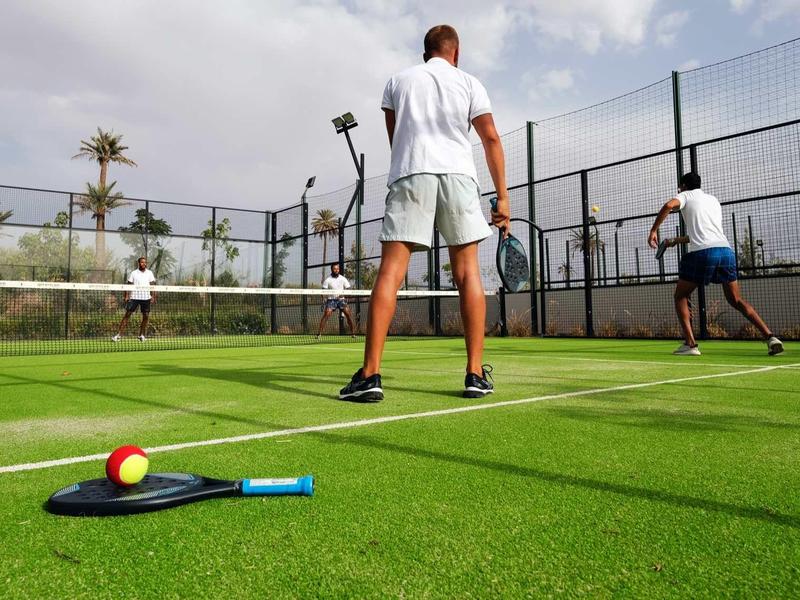 Dva muži hrají paddle tenis na venkovním hřišti za zatažené oblohy.