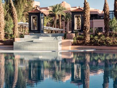 Area piscina moderna con sculture e palme di fronte a un edificio alberghiero.