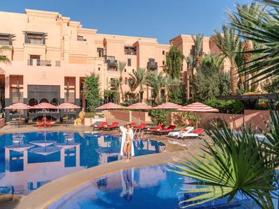 Hotel con area piscina tropicale, lettini e ombrelloni sotto un cielo blu