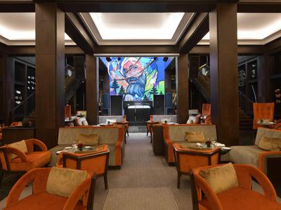 Accogliente hall d'hotel con poltrone arancioni e TV a parete.