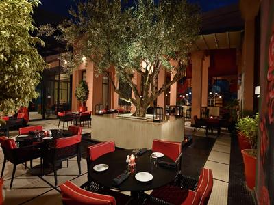 Ristorante elegante con tavoli rotondi, sedie rosse e albero centrale di notte.