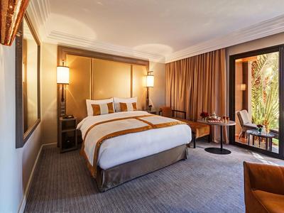 Camera d'hotel accogliente con letto grande, due comodini e accesso al balcone con vista sul giardino.