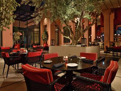 Ristorante elegante con sedie rosse e grandi alberi in un cortile aperto.