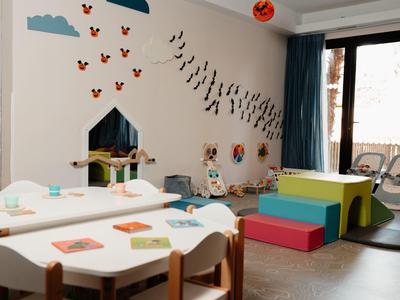 Sala giochi per bambini con tavoli, sedute a cubo colorate e decorazioni murali sotto una luce calda.