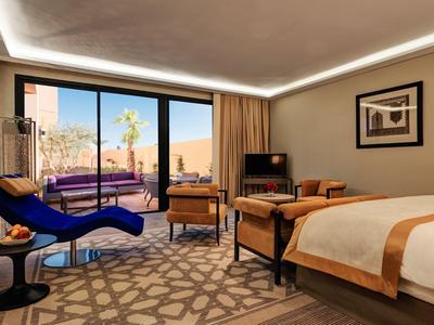 Elegante camera d'hotel con letto grande, zona salotto e balcone con vista su deserto e piscina