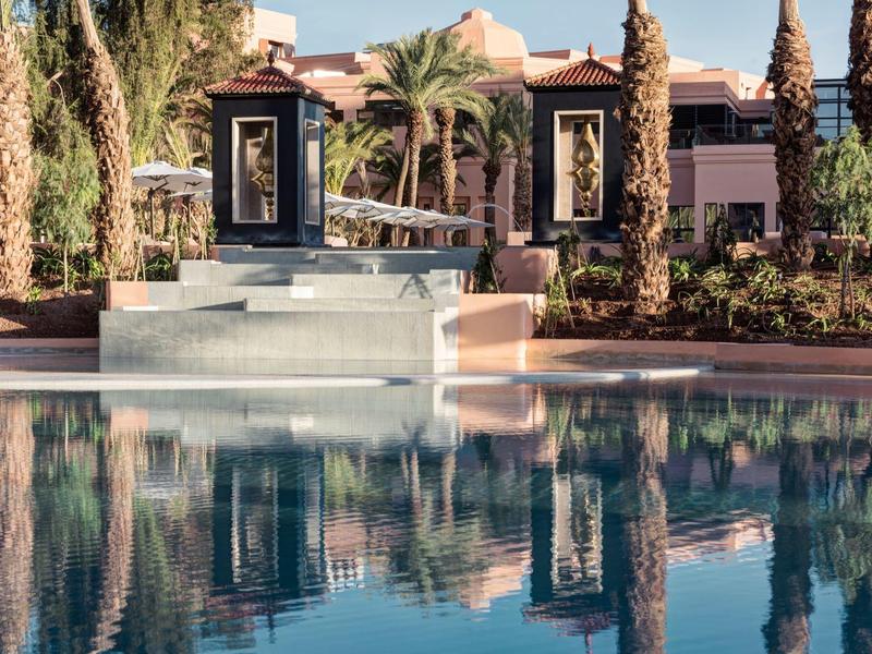 Piscina di lusso con palme e sculture davanti a un edificio dell'hotel al sole.