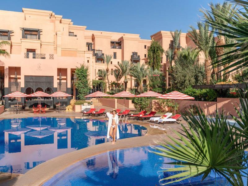 Hotel con grande piscina, lettini e ombrelloni davanti a un edificio di più piani sotto un cielo blu