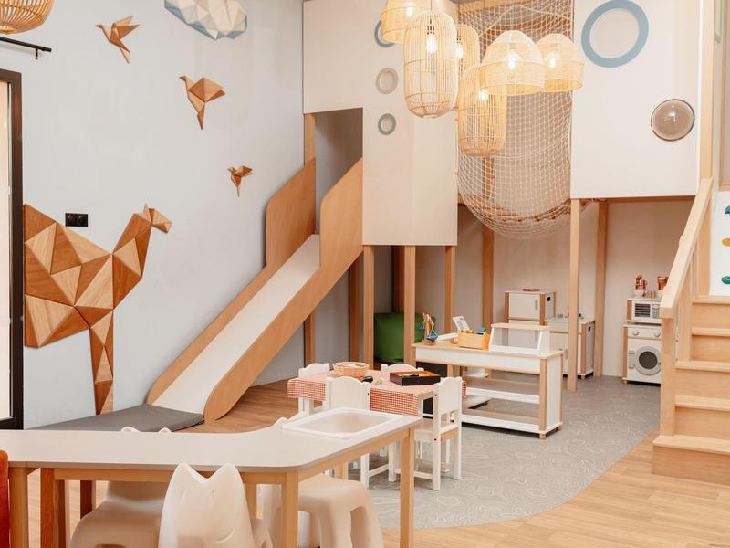 Area giochi per bambini con giocattoli di legno, scivolo e decorazioni murali nell'interno di un hotel.