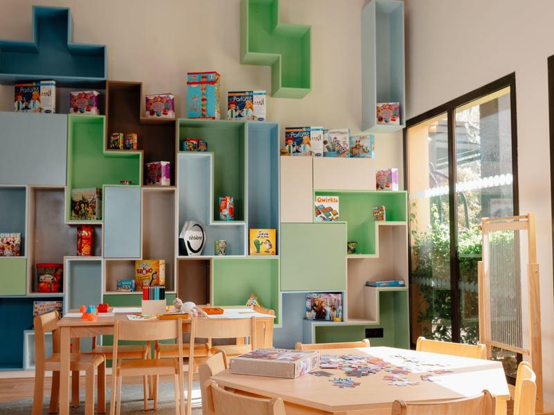 Stanza luminosa con scaffali colorati a parete, tavoli e sedie per bambini, luce naturale