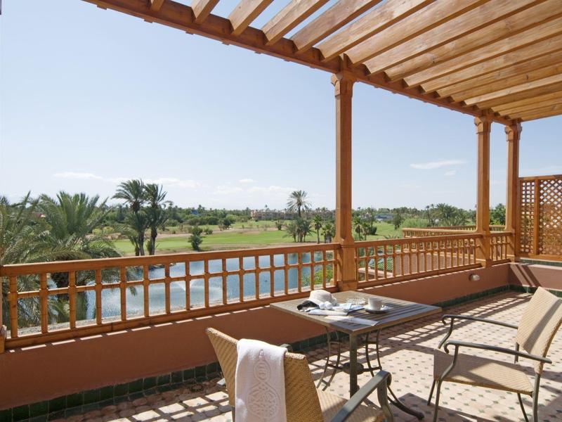 Balkon z drewnianym dachem i stołem z krzesłami z widokiem na zielony krajobraz z palmami.