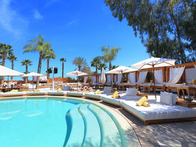 Luksusowy basen z białymi leżakami, parasolami i palmami pod czystym niebem.