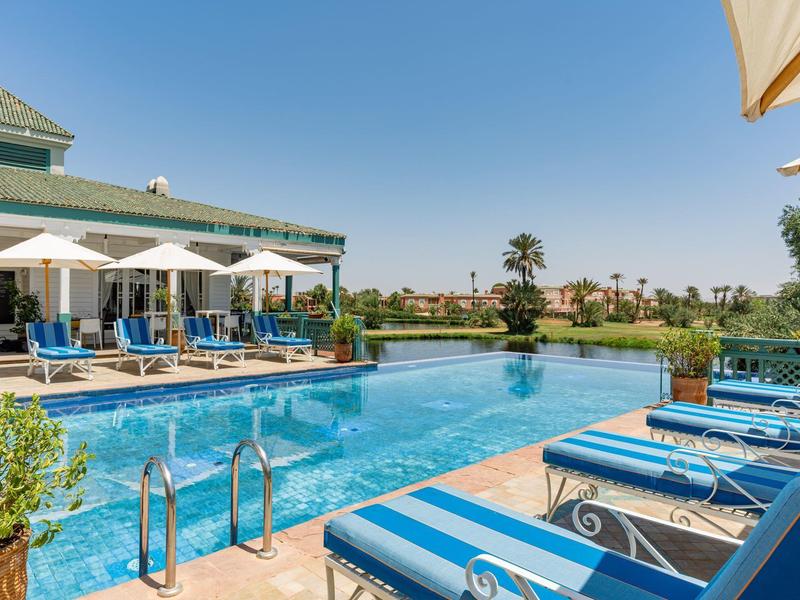 Duży basen z niebieskimi leżakami i parasolami obok hotelu pod czystym niebem.