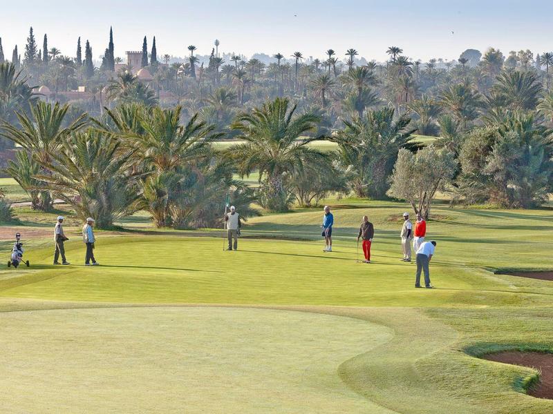 Zielone pole golfowe z graczami i palmowymi wzgórzami w tle