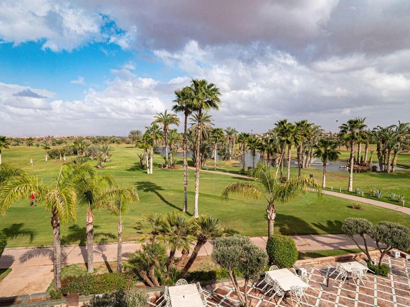 Zielone pole golfowe z palmami pod pochmurnym niebem z niebieskimi przebłyskami.