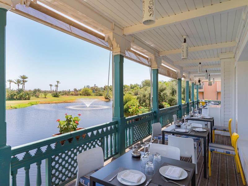 Taras z nakrytymi stołami z widokiem na jezioro i palmy w oddali.