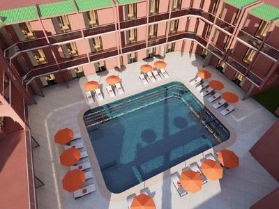 Innenhof eines Hotels mit rechteckigem Pool und orangen Sonnenliegen auf weißem Boden.